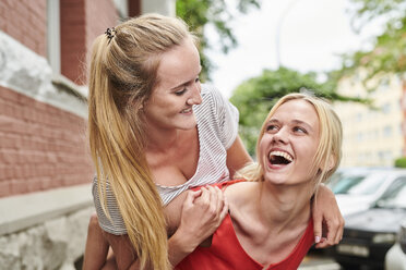 Happy young woman giving friend piggyback ride in the city - MMIF00168
