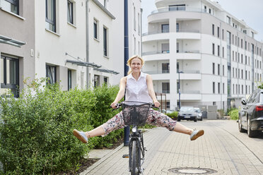 Happy young woman riding bicycle in housing area - MMIF00174