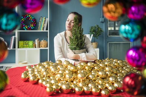 Frau sitzt an einem Tisch mit vielen goldenen Weihnachtskugeln und hält einen Tannenbaum in der Hand - MOEF01336