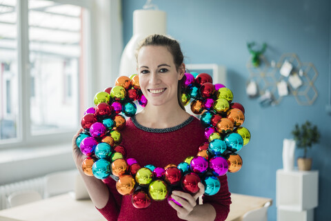 Porträt einer lächelnden Frau mit buntem Weihnachtskugelkranz, lizenzfreies Stockfoto