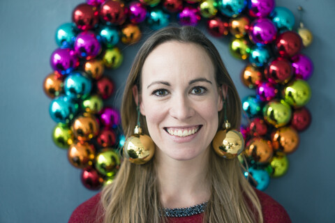 Porträt einer lächelnden Frau mit goldenen Weihnachtskugel-Ohrringen, lizenzfreies Stockfoto