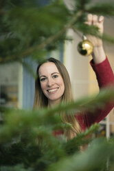 Porträt einer lächelnden Frau beim Schmücken des Weihnachtsbaums - MOEF01346
