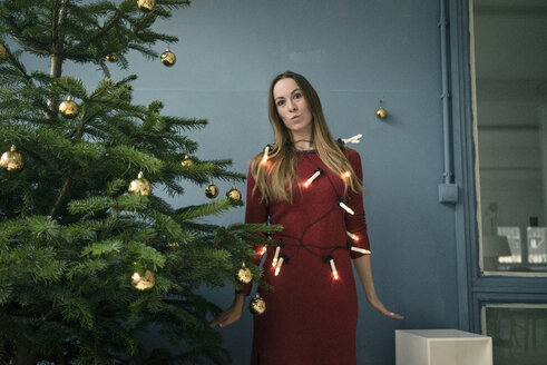 Porträt einer Frau mit Lichterkette, die neben einem Weihnachtsbaum steht - MOEF01353