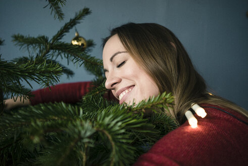 Glückliche Frau, die den Weihnachtsbaum umarmt - MOEF01358