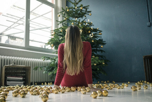 Rückenansicht einer Frau, die mit vielen goldenen Weihnachtskugeln auf dem Boden sitzt und den Weihnachtsbaum betrachtet - MOEF01361