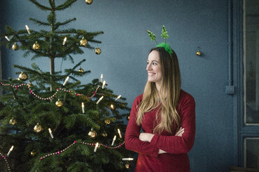 Content woman with Christmas headdress standing besides decorated Christmas tree - MOEF01365