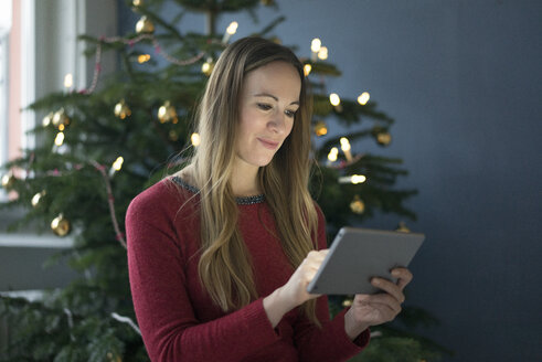 Porträt einer lächelnden Frau, die zur Weihnachtszeit ein Tablet benutzt - MOEF01368