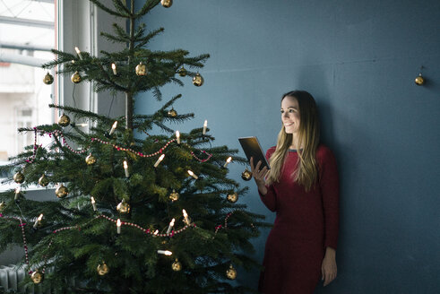 Lächelnde Frau mit Tafel neben geschmücktem Weihnachtsbaum - MOEF01369