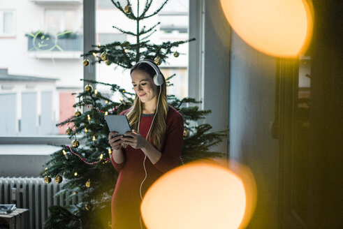 Lächelnde Frau mit Tablet und Kopfhörern zur Weihnachtszeit - MOEF01373