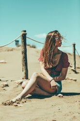 Young woman sitting on sandy beach - OCAF00250