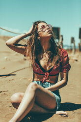 Young woman sitting on sandy beach - OCAF00251