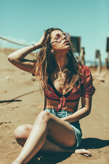 Junge Frau sitzt am Sandstrand - OCAF00251