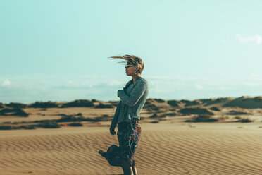Young woman with windswept hair standing in desert landscape - OCAF00258