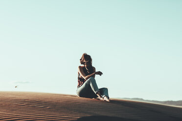 Junge Frau sitzt in Wüstenlandschaft - OCAF00271