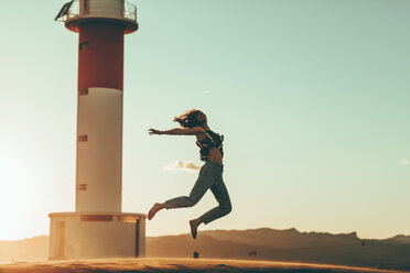 Junge Frau springt in Wüstenlandschaft am Leuchtturm - OCAF00275