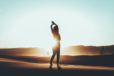 Silhouette of woman standing in desert landscape at sunset - OCAF00279