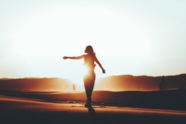 Silhouette of woman standing in desert landscape at sunset - OCAF00280