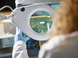 Female technician checking circuit board with magnifier - CVF00703