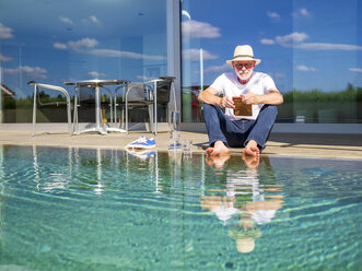 Senior man reading e-book at swimming pool - LAF02046