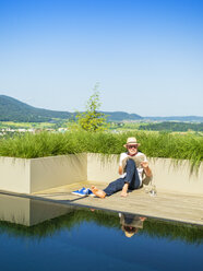 Senior man reading newspaper at swimming pool - LAF02053