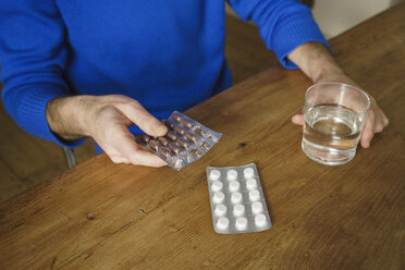 Midsection of man taking medicine with water at table - FSIF03122