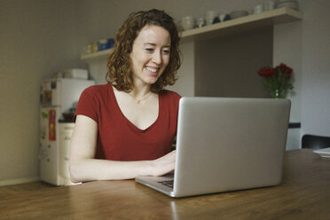 Smiling woman sitting at table using laptop in kitchen - FSIF03124