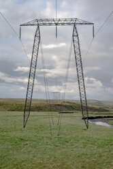 Reihe von Strommasten auf grüner Wiese gegen bewölkten Himmel, Hochland, Island - FSIF03141