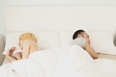 Young couple lying back to back on bed at home - FSIF03155