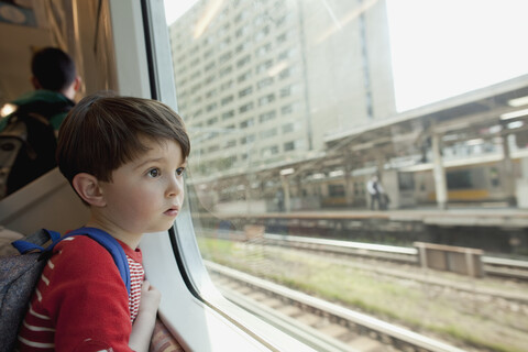 Neugieriger Junge, der durch ein Glasfenster schaut, während er im Zug reist, lizenzfreies Stockfoto