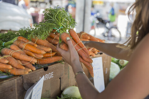 Frau am Obst- und Gemüsestand bei der Auswahl von Karotten, lizenzfreies Stockfoto