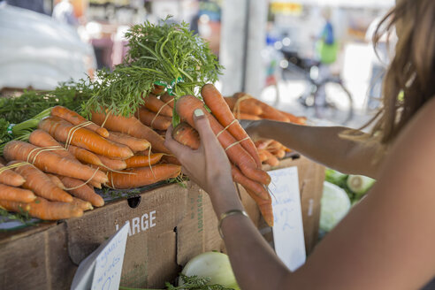 Woman at fruit and vegetable stall selecting carrots - ISF09245