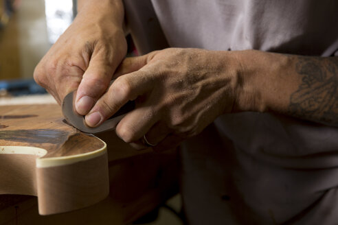 Guitar maker in workshop sanding guitar - ISF09319