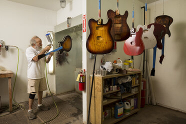 Guitar maker in workshop using spray gun to varnish guitar - ISF09320