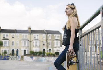 Young female skateboarder leaning against fence in skatepark - CUF23165