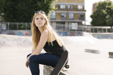 Portrait of young female skateboarder sitting in skatepark - CUF23168