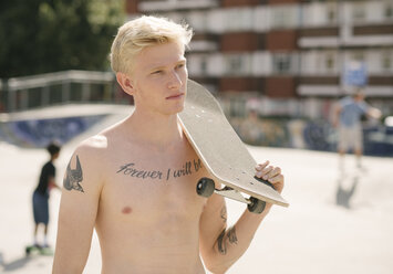 Tätowierter junger Mann trägt Skateboard auf der Schulter im Skatepark - CUF23171