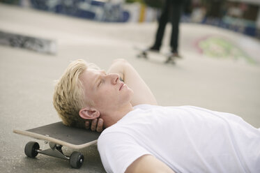 Junger männlicher Skateboarder liegt mit geschlossenen Augen im Skatepark - CUF23172