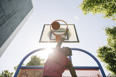 Junger männlicher Basketballspieler wirft den Ball in den sonnenbeschienenen Basketballkorb - CUF23182