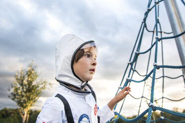 Porträt eines Jungen im Astronautenkostüm, der am Klettergerüst auf dem Spielplatz steht - CUF23193