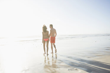 Rückansicht eines jungen Paares in Badekleidung, das am sonnenbeschienenen Strand spazieren geht, Kapstadt, Westkap, Südafrika - CUF23199