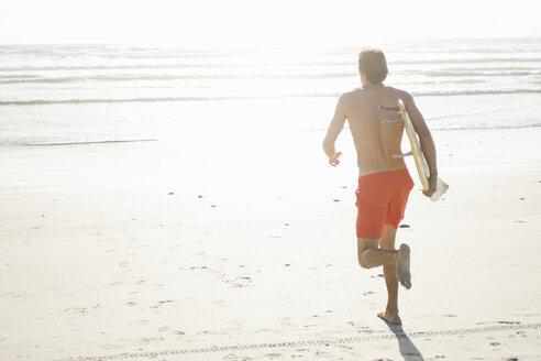 Rückansicht eines jungen männlichen Surfers, der am sonnenbeschienenen Strand läuft, Kapstadt, Westkap, Südafrika - CUF23207