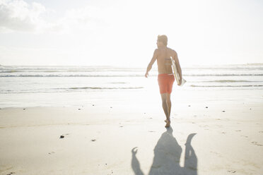 Rear view of young male surfer running on sunlit beach, Cape Town, Western Cape, South Africa - CUF23208