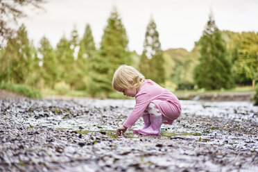 Baby girl wearing rubber boots playing in muddy puddle - CUF23216