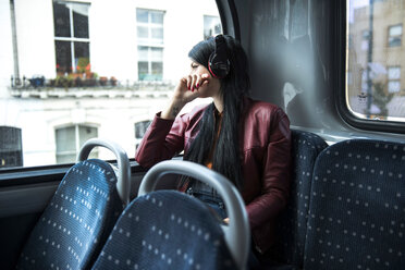 Young woman sitting on bus, wearing headphones, looking out of window - CUF23235