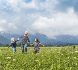 Großmutter und Enkelkinder laufen händchenhaltend im Feld, Füssen, Bayern, Deutschland - CUF23248