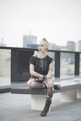 Porträt eines jungen weiblichen tätowierten Punks, der auf dem Dach einer Mauer sitzt - CUF23256