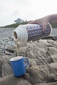 Female hand pouring tea from drinks flask on Millook Beach, Cornwall, UK - CUF23287