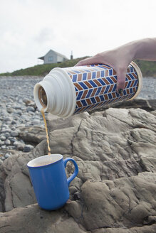 Weibliche Hand gießt Tee aus einer Trinkflasche am Millook Beach, Cornwall, UK - CUF23287