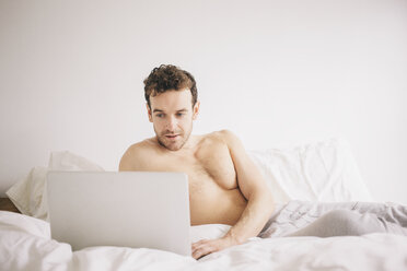 Young man lying in bed using laptop - CUF23315
