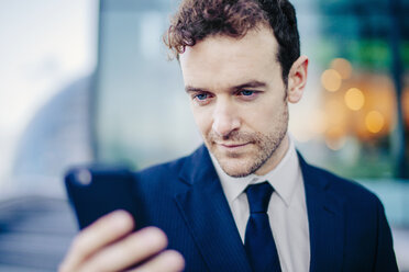 Businessman texting on smartphone in front of office - CUF23317